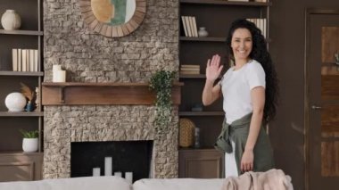 Neşeli, neşeli, neşeli, neşeli genç kadın kameraya bakıyor gülümsüyor, selamlıyor, komik selamlıyor, kanepenin arkasına saklanıyor, modern apartman dairesinde eğleniyor, mizah kavramı oynuyor.