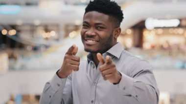 Yakından mutlu, yakışıklı, Afro-Amerikalı bir adam kameraya bakıp gülümsüyor ve jest yapıyor. Siz tabancalar seçim onayı işareti yapıyorsunuz.