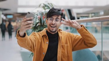Genç yakışıklı Arap adam blogger model elinde telefonla cep telefonuyla poz verirken gülümseyerek fotoğraf çekerken akıllı telefondaki blog için video çekerken görüntülendi.