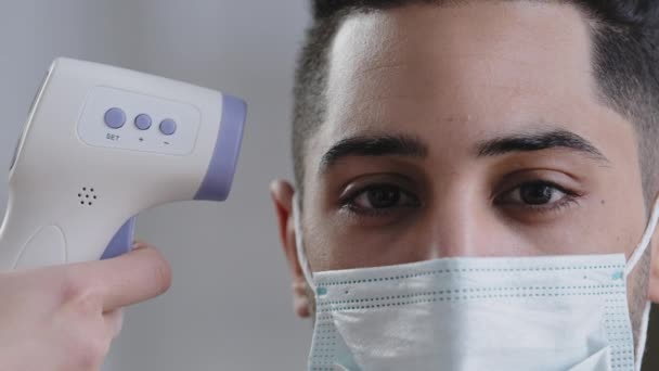 Scanner a infrarossi con visione ravvicinata su clienti maschi uomo arabo in maschera medica protettiva scansione della temperatura corporea paziente misurazione della febbre tramite termometro elettronico digitale covid-19 controllo — Video Stock