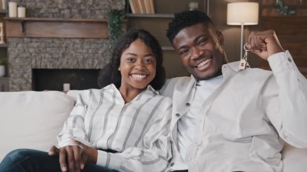 Afrikanisches Ehepaar sitzt in modernem Wohnzimmer im neuen Heim Frau und Mann zeigen Schlüsselbund von neuen Luxus-Haus-Wohnung gemietet. Eigenheimbesitzer mit Hypothekenkredit — Stockvideo