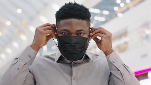 Close-up young african american man wears protective medical mask observes precautionary measures during pandemic looks at camera shows ok gesture approval symbol sign agreement protect your health — ストック動画
