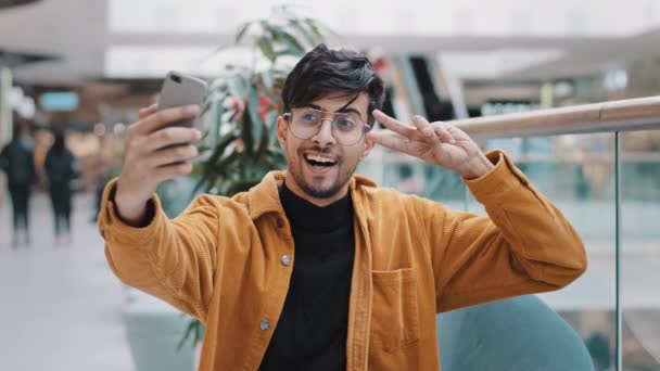 Νεαρός όμορφος arab τύπος blogger μοντέλο κρατώντας τηλέφωνο στο χέρι φωτογραφήθηκε στο κινητό κάμερα ποζάροντας χαμογελώντας κάνοντας χειρονομία λήψη φωτογραφιών κινηματογράφηση βίντεο για το blog στο smartphone χρησιμοποιώντας εφαρμογή βίντεο chat — Αρχείο Βίντεο