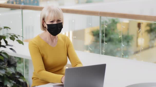 Fokuserad förbryllad mogen kaukasisk kvinna i skyddande mask skriva på bärbar dator upprörd gör misstag klamra huvudet med händerna känner stress sorg över problem att förlora online-spel dåligt beslut — Stockvideo