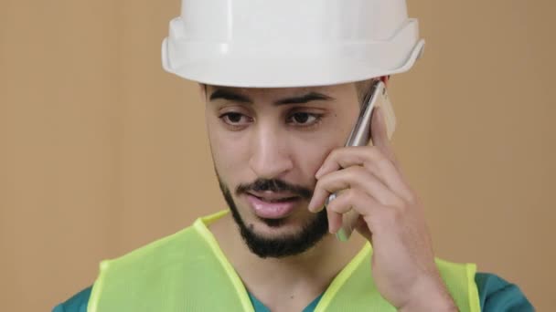 Gros plan du jeune ingénieur hispanique constructeur de contremaître de construction en casque de sécurité spécial parlant téléphone portable avec travailleur du bâtiment discutant fond de plan néon éclairage d'urgence — Video