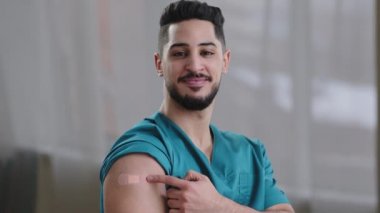 Omuz enjeksiyonu aşısı üzerindeki yamayı gösteren kameraya bakarak Coronavirus enfeksiyonunun bağışıklık sistemini uyaran kovid 19 virüsünden etkilenmiş Arap erkek doktor.