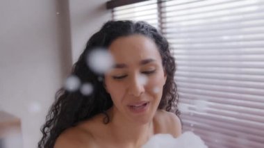 Komik, neşeli, neşeli, çıplak, güzel bir kadın banyoda oynuyor, gülümsüyor, gülüyor, etrafta gülüyor, küvette dinleniyor, sabunla eğleniyor, eğleniyor.