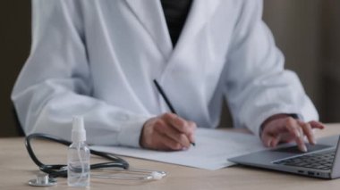 Bilinmeyen bir sağlık çalışanının hastane masasında tıbbi malzeme terapisti kadın el yazısı notlarıyla birlikte günlük hastane çalışma konseptinde dizüstü bilgisayarda yazı yazması.