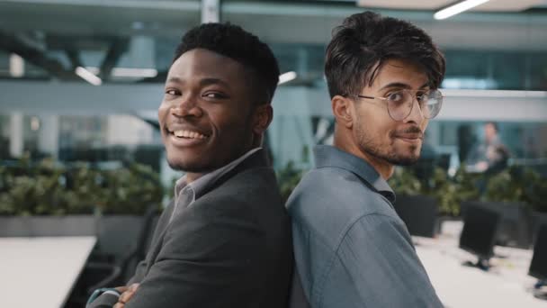 Porträtt två multinationella manliga kollegor män afrikansk man arabiska indiska chef poserar i kontorsföretag står tillbaka till varandra partnerskap tittar på kameran ler affärspartners anställda — Stockvideo