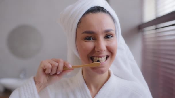 Close-up młoda kobieta z ręcznikiem na głowie po prysznicu szczotkowanie zdrowe białe zęby z pasty do zębów szczoteczki usta ze szczoteczką do zębów w domu łazienka rano rutynowa opieka stomatologiczna higieny osobistej pojęcie — Wideo stockowe