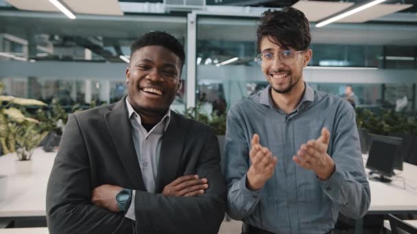 İki neşeli iş arkadaşı Afrikalı Arap satıcı kameraya bakıp gülüyor. Komik iş durumu. Çalışma alanındaki şirket şakası. — Stok video