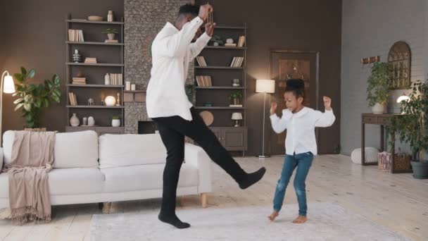 Amante papá africano bailando con hija linda del niño en la sala de estar padre feliz y niña pequeña jugando saltar piernas en movimiento activo a la música disfrutar de fiesta de baile despreocupado tiempo de vacaciones juntos en casa — Vídeos de Stock