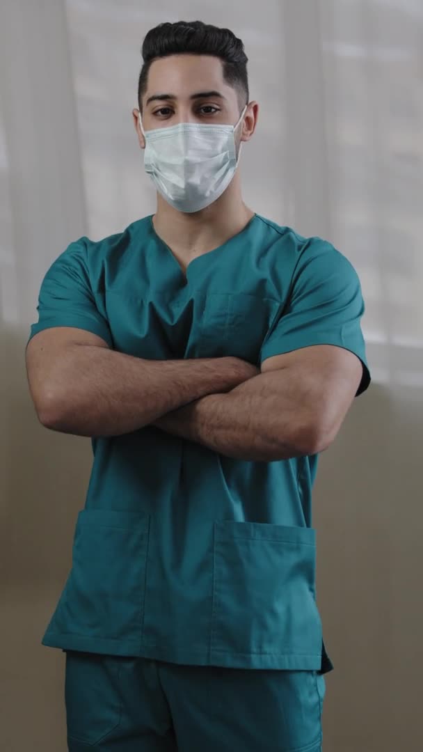 Dikey görüşlü Hintli maskeli doktor hemşire üniformalı doktor hastanede kollarını kavuşturup hasta tedavisine hazır bir şekilde poz veriyor. — Stok video