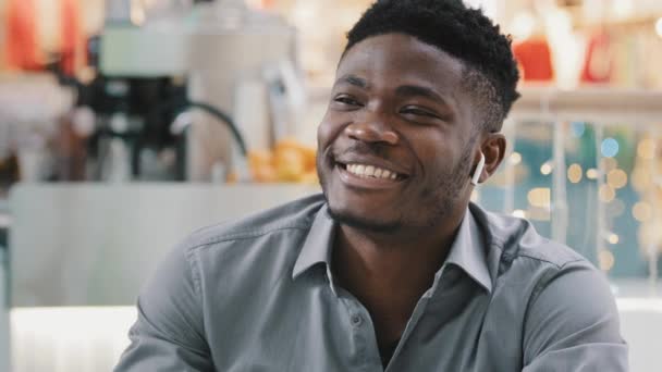 Close-up joven afroamericano feliz hablando a través de auriculares inalámbricos sonriendo respondiendo amigable llamada de negocios comunicándose explicando el chat con amigos de forma remota utilizando tecnología moderna — Vídeo de stock