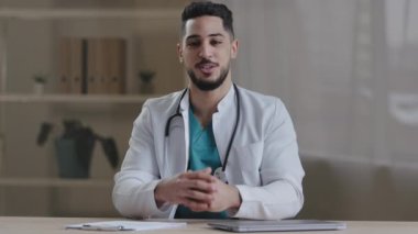 Neşeli gülümseyen genç adam, steteskoplu pratisyen doktor kameraya konuşuyor. Teşhisin detaylarını açıklıyor. Görüntülü arama danışmanlığı, sağlık hizmetleri web kamerası görüntülerini kaydediyor.