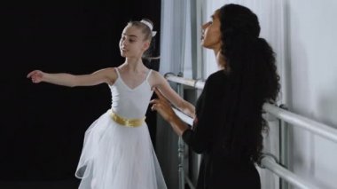 Beyaz kız öğrenci balerin, bale barının yanında dans egzersizleri yapıyor. Koreografi eğitimi alan yetişkin öğretmen bayan eğitmenin açıklamalarını dinliyor.