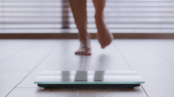 Närbild smala kvinnliga ben oigenkännlig kvinna promenader barfota över rummet kliva på elektroniska skalor kontrollera vikt efter fettförbränning träning hemma kroppskontroll viktminskning kost livsstil — Stockvideo