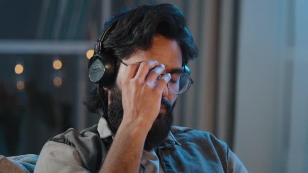 Portré arab multiraciális férfi Y-generációs srác 30-as férfi szakállas barna fülhallgató ül otthon éjszaka sötét este pihenő szünet végén kemény munka nap élvezi a zene kiváló minőségű hang dal — Stock videók