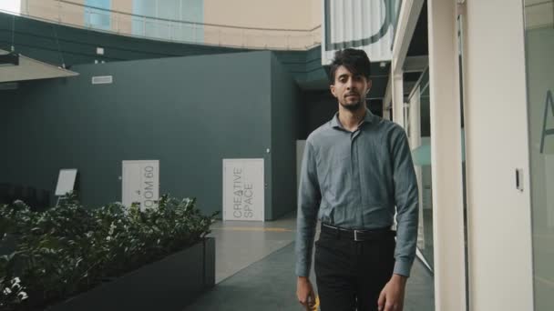 Genç, ciddi Arap girişimci yönetici patron modern, modern koridor ofisinde yürüyen ve cam duvar arkaplanının yakınındaki kameraya bakarak kendine güvenen iş adamı portresi. — Stok video