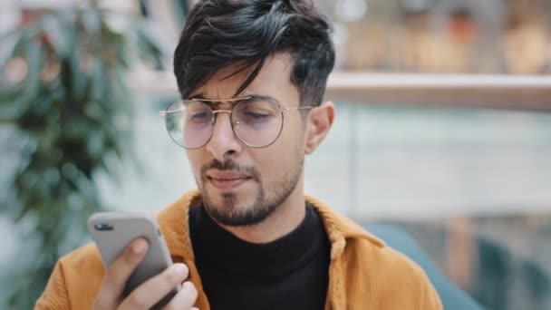 肖像画を心配し、若いアラブ人の男が屋内で電話に応答コールで話す立っているスマートフォン男怒って悪い携帯電話サービスモバイル接続の問題低バッテリー壊れた携帯電話のマイク — ストック動画