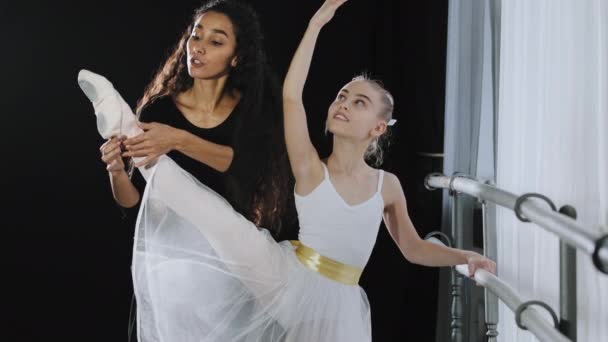 Chica adolescente concentrada aprendiendo danza de ballet en estudio con profesora entrenadora ayuda a estirar la pierna de pie en pose de ballet apuntando con el dedo del pie entrenamiento de danza con sofá mujer bailarina practicando educación artística — Vídeos de Stock