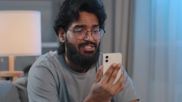Arab man bearded guy indian male blogger video call conference remote conversation at home talking in smartphone webcam recording video blog vlog online broadcast stream distant friendly communication — ストック動画