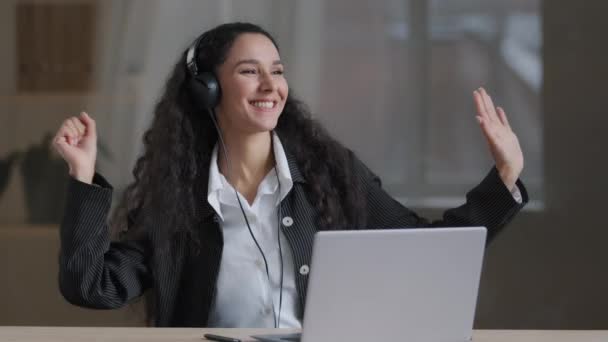 Щаслива молода арабська леді-фрілансерка в навушниках слухає гучну музику в навушниках, вільно співаючи в офісі, розслабляючи плавні рухи рук, марнуючи час на робочому місці, приймаючи концепцію перерви на роботі — стокове відео
