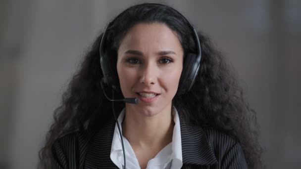 Front view of young hispanic lady stress resistant bank worker operator looking at camera in headphones with microphone answer incoming call clients provide support service customers telesales concept — ストック動画