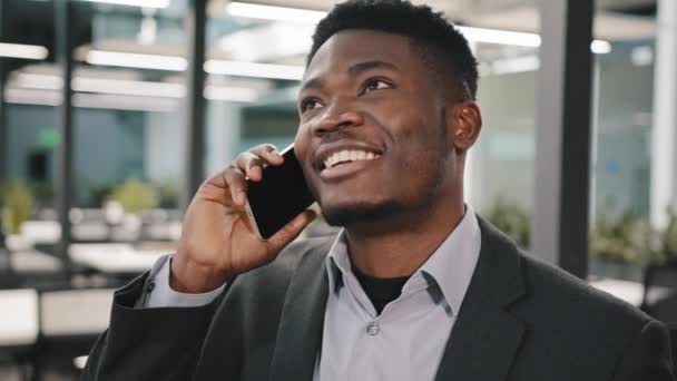 Afrikaanse business analist manager glimlachende man spreken op mobiele telefoon klant consulting communiceren emotioneel indoor vertellen verhaal maken online bestelling regelen vergadering collega in leeg kantoor — Stockvideo