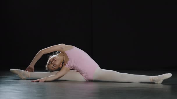 Подросток талантливый гибкий профессиональный акробат балерина танцовщица ребенок, сидящий на полу на сплит бечевки склоняясь в сторону растяжения практикуя акробатические гимнастические элементы обучения в танцевальном классе — стоковое видео