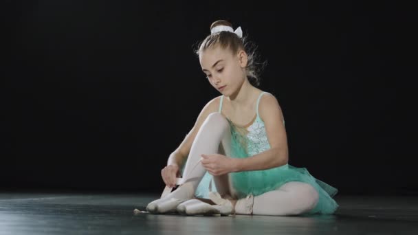 Юная кавказка в балетной обуви сидит на галстуках на лентах пуантовых туфель юная балерина готовится к занятиям танцами одетая в балетную обувь элегантная танцовщица, готовая к танцам — стоковое видео