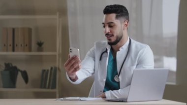 Erkek doktor genel doktor İspanyol doktor hastane dolabındaki mobil teletıp uygulaması aracılığıyla müşterilerine danışmanlık yapıyor. Sağlık hizmetleri konseptiyle uzaktan iletişim kuruyor.