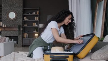 Genç, mutlu bir kadın yatak odasında oturuyor. Bavullarını bavula koyuyor. Tatil için seyahate çıkıyor.