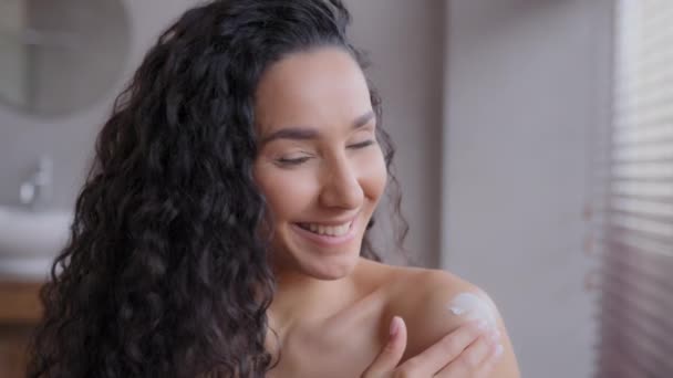 Headshot joven feliz mujer sonriente aplicando crema hidratante sentado en el baño disfrutando del spa doméstico diario poniendo crema hidratante cosmética orgánica loción haciendo cuidado de la piel corporal diaria concepto de cuidado de la piel — Vídeo de stock