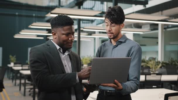 Dos hombres socios de negocios hombres hombre árabe celebración de la computadora portátil que muestra la presentación hombre de negocios africano mirando a los colegas de la pantalla de ordenador que trabajan en línea discutir inicio apuntando pantalla haciendo elección — Vídeos de Stock