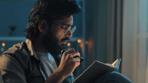 Arab indiai felnőtt férfi szakállas szemüveges ül otthon késő este sötétség blackout olvasás lelki könyv tankönyv zseblámpával otthoni tanulás tanulás felkészülés vizsgák — Stock videók