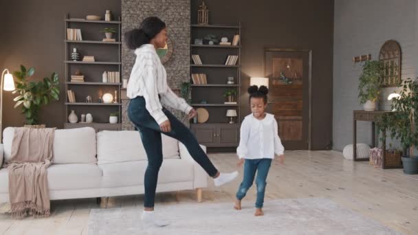 Aktiv afrikansk mor babysitter amerikansk energisk lille barn datter hoppe dans i huset stue lykkelig mor med barn pige have det sjovt sjove dans spil musik bevægelse nyde at spille derhjemme – Stock-video