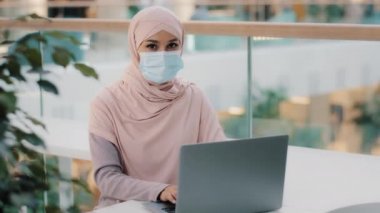 Tıbbi maskeli genç Arap kadın yeni bilgisayar uygulamasını onaylayan dizüstü bilgisayarla çalışıyor. Onaylanmış jestler gösteriyor ki, hizmet iyi tavsiye reklam sistemiyle mutlu olmuş.