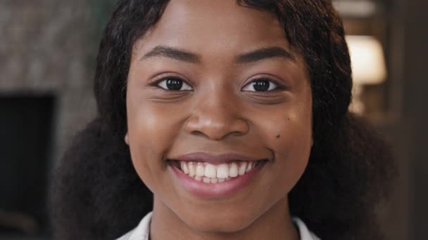 Extreme close-up vrouwelijk gezicht met perfecte huid gezonde duizendjarige Afrikaanse vrouw op zoek naar camera binnen gelukkig jaren '20 meisje met witte tanden glimlach in appartement lachend casual model poseren portret — Stockvideo