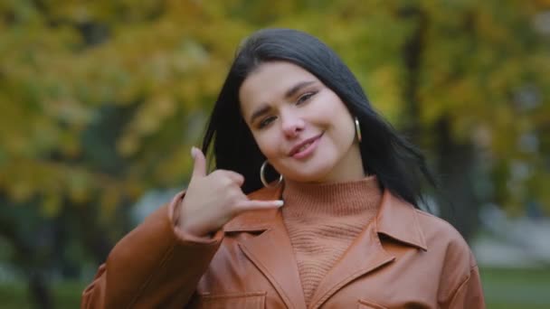 Close-up jonge mooie Latijns-Amerikaanse vrouw in het park poseren buiten kijken naar camera met hand gebaar telefoon in de buurt van oor demonstreren teken bel me bellen symbool aanbieden van communicatie flirten — Stockvideo