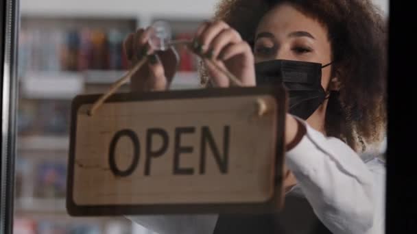 View through glass door young woman owner waitress in medical protective mask in apron closes store restaurant turns sign that says CLOSED business during quarantine economic crisis security measures — Stock Video
