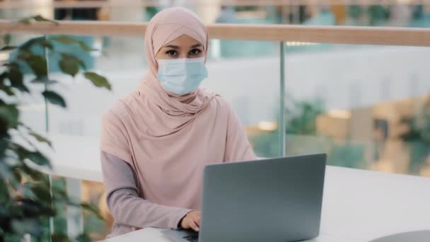 Jeune femme arabe en hijab dans le masque médical fonctionne sur ordinateur portable approuvant une nouvelle application informatique montre geste pouce vers le haut démontre signe de consentement heureux avec le service bonne recommandation système de publicité — Video