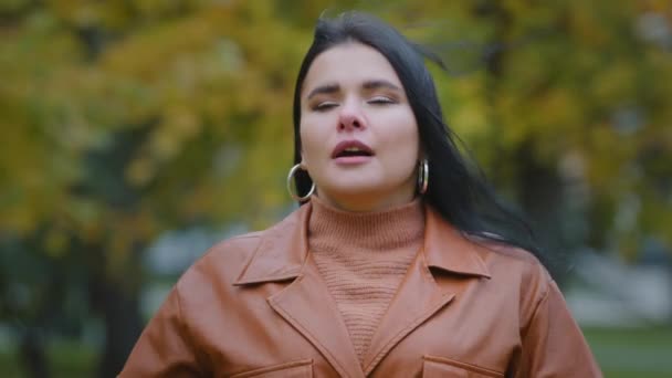 Молода іспаномовна жінка, що стоїть на відкритому повітрі, чхає в носову хустку, витираючи ніс, відчуваючи погану хворобу сезонну холодну алергію, що страждає від хвороби корози симптоми грипу респіраторного вірусу — стокове відео