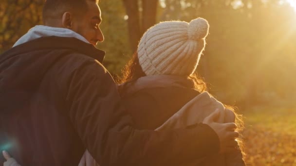 Θέα από πίσω γκρο πλαν νεαρό ερωτευμένο ζευγάρι στο πάρκο του φθινοπώρου αγκαλιάζοντας χαριτωμένες κουβέντες απολαμβάνοντας ευχάριστο παιχνίδι μαζί θαυμάζοντας τη θέα του ηλιοβασιλέματος απολαμβάνοντας την τελευταία ζεστή ηλιαχτίδα που στέκεται στην αγκαλιά — Αρχείο Βίντεο