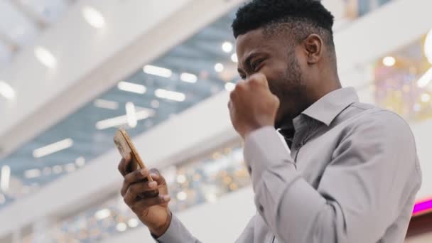 Fiatal boldog elégedett afro-amerikai srác győztes nézi a telefon képernyőjén ünneplő győzelem siker mosolygós online szerencsejáték olvasni jó hír a mobiltelefon nyer lottó kapott álom munka promóció — Stock videók