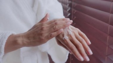 Kapalı kadın elleri. Bornozlu, tanınmayan sağlıklı genç kadın nemlendirici sürüyor. Kuru kollar için besleyici nemlendirici losyon sürüyor.