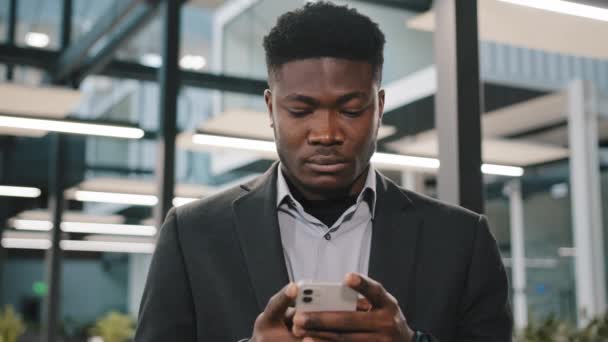 Ciddi Afro-Amerikan ofis çalışanı akıllı telefon internetini araştırıyor. Arkadaşlarıyla çevrimiçi sohbet etmeyi seçiyor. Düşünceli erkek kullanıcı tarayıcı hesabına tıklıyor. — Stok video