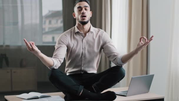 Уважний спокійний арабський працівник бізнесу в позі лотоса сидить на робочому столі закриті очі, роздумуючи зробити перерву в домашньому офісі, тримати розумовий баланс терпіння йога практики ніякого стресу відчувати баланс дзен — стокове відео