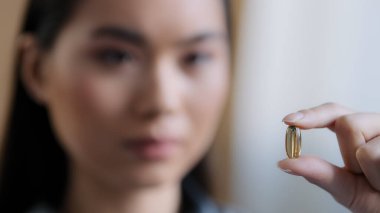 Yakın plan Asyalı hasta kız kendini iyi hissetmiyor balık yağı kapsülü tutuyor besleyici ilave ilaç tedavisi için ağrı kesiciler için ilaç kullanıyor Omega 3 'lü tıbbi tedaviyi düşünüyor.