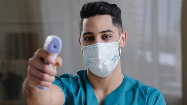 Arabian male medical worker doctor surgeon man in protective mask taking temperature with non-contact infrared digital thermometer during covid-19 pandemic controlling disease symptoms coronavirus